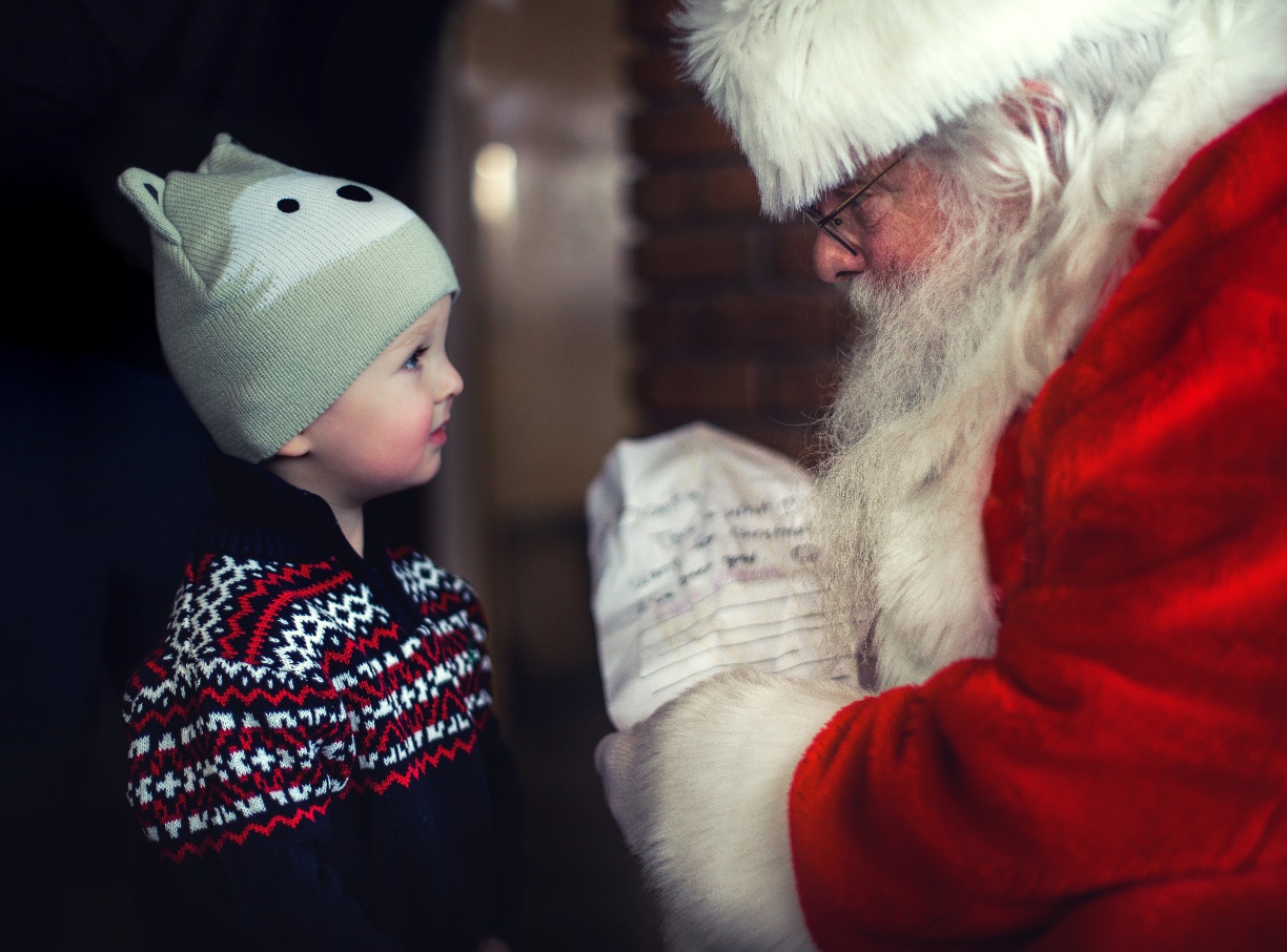 Santa Claus checking his list while talking with a little boy
