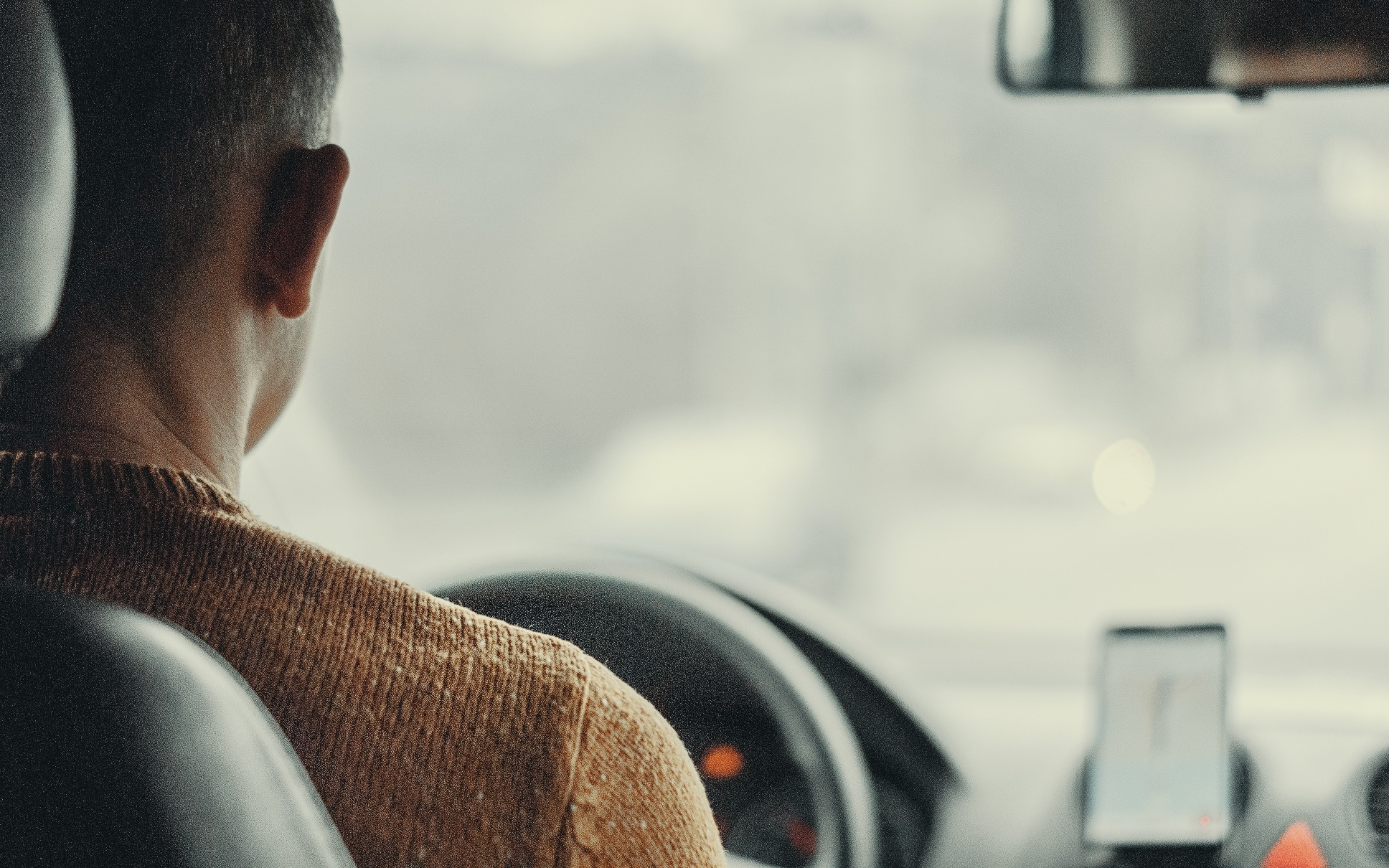 A person wearing a yellow shirt driving a car. 